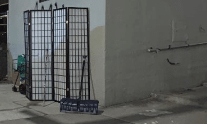 A picture of a room divider screen on a sidewalk near a wall, A snow shovel is in front and a bit of a shopping cart of some kind is peeking out from the left side.