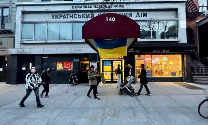 a building on a city sidewalk with a number of people walking in front.