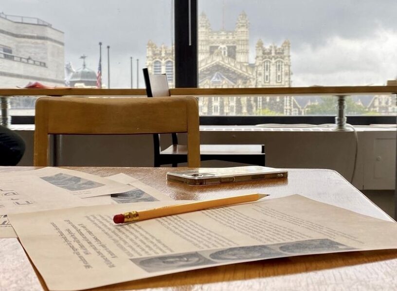 Perspective of papers scattered across a desk along with a phone and pencil.