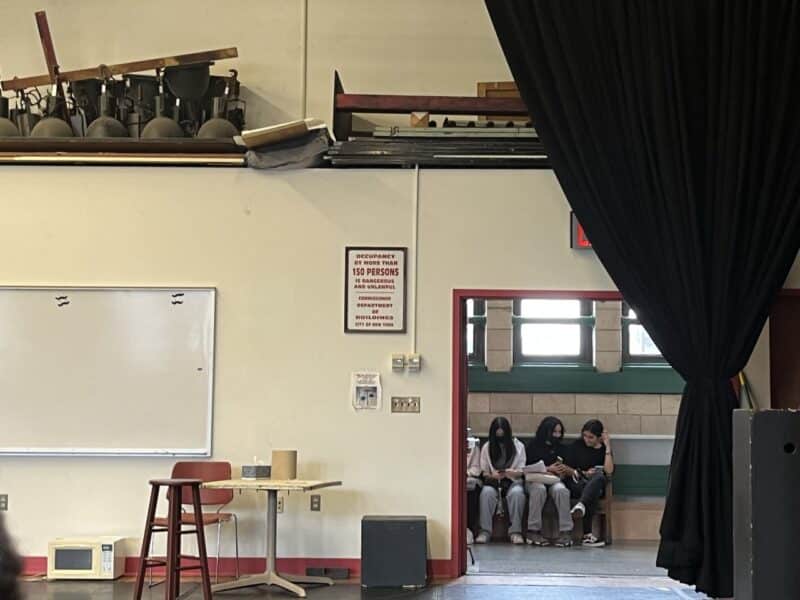 Perspective shot of students seated on a bench inside a theater room waiting for instructions.